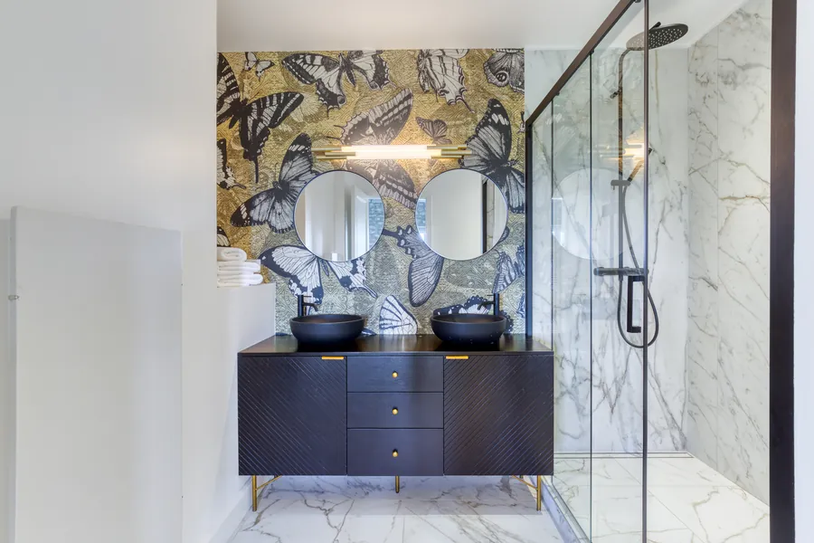 A bathroom with butterfly mosaic wall, twin round mirrors and marble shower