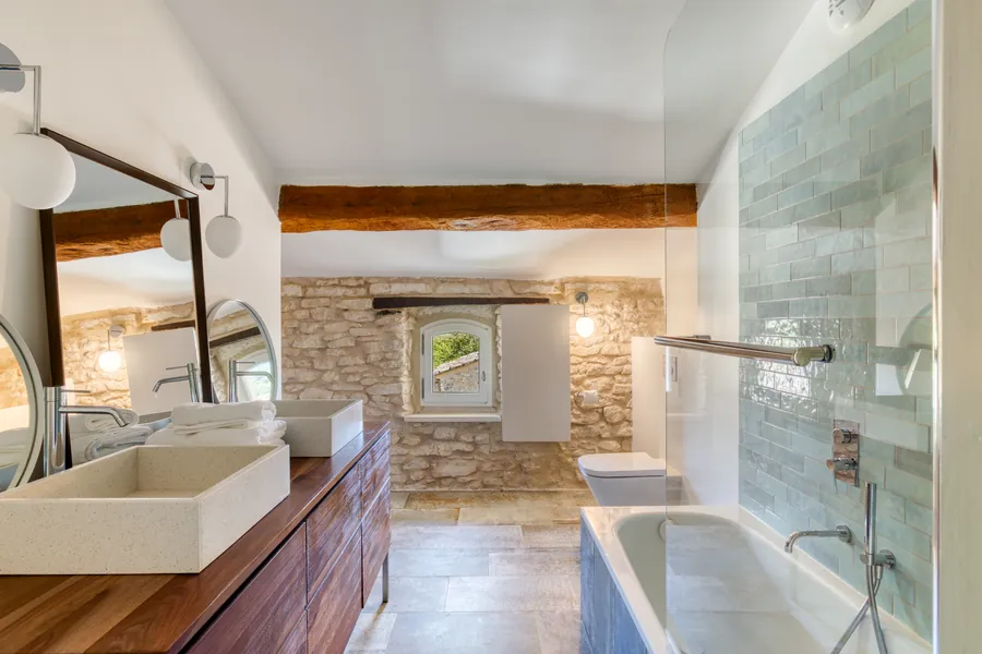 A bathroom with stone walls, a walnut vanity and a tiled bath
